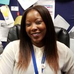 This is a picture of our principal, Ms. Jovan Moore. She is smiling at her desk, in her office.