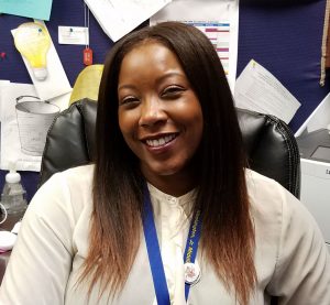This is a picture of our principal, Ms. Jovan Moore. She is smiling at her desk, in her office.