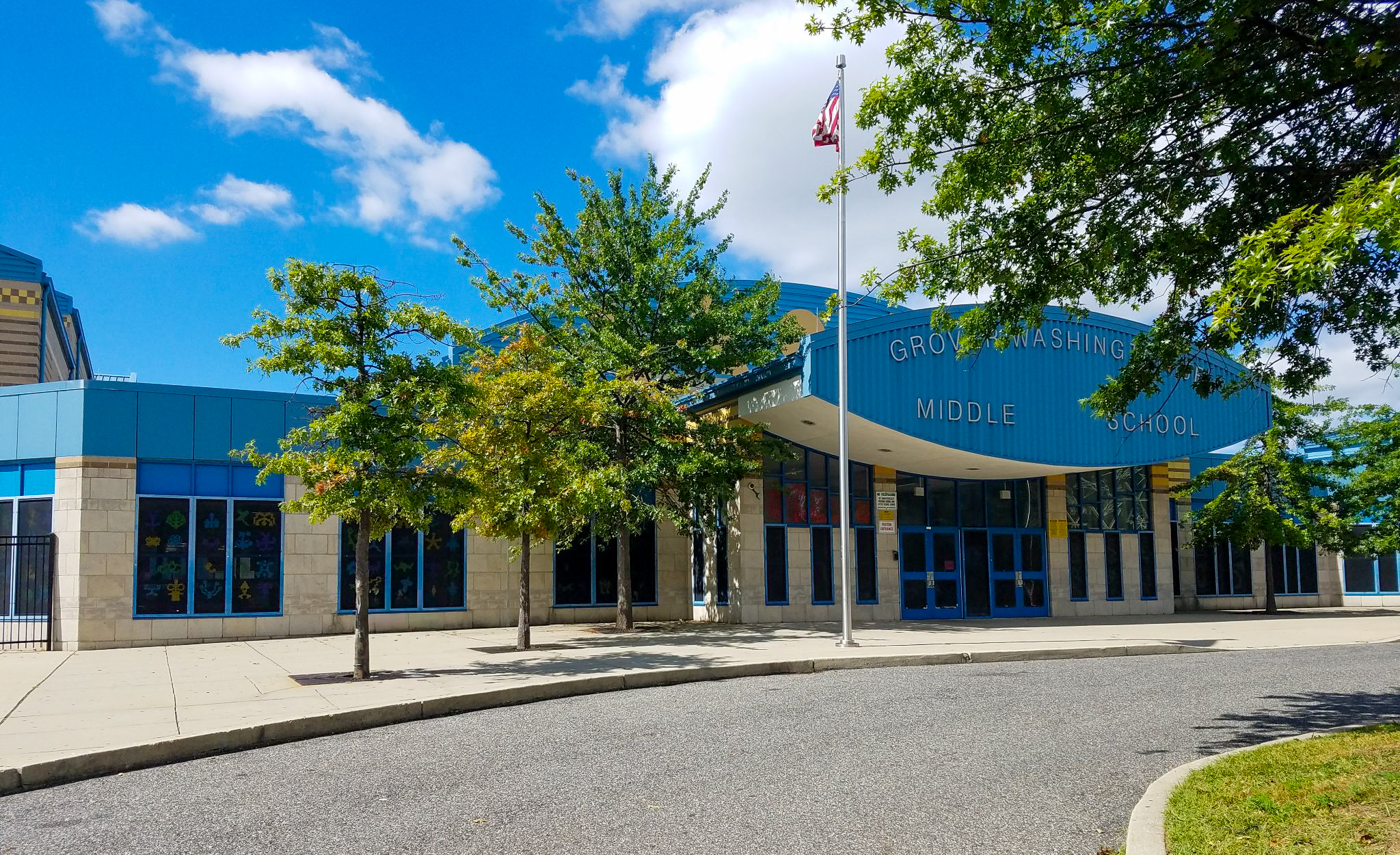Exterior of Grover Washington Jr. Middle School with trees and an American flag near the main entrance.
